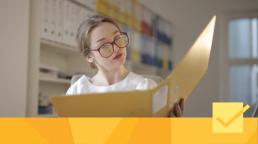 A woman wearing red glasses reading a binder of peer review reports to improve her research paper.