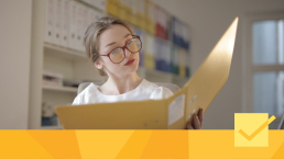 A woman wearing red glasses reading a binder of peer review reports to improve her research paper.