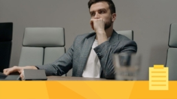 A man in a grey suit sitting at a desk solo managing a journal.